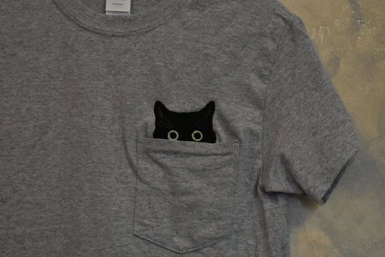 Gray t-shirt with black cat poking head out of pocket